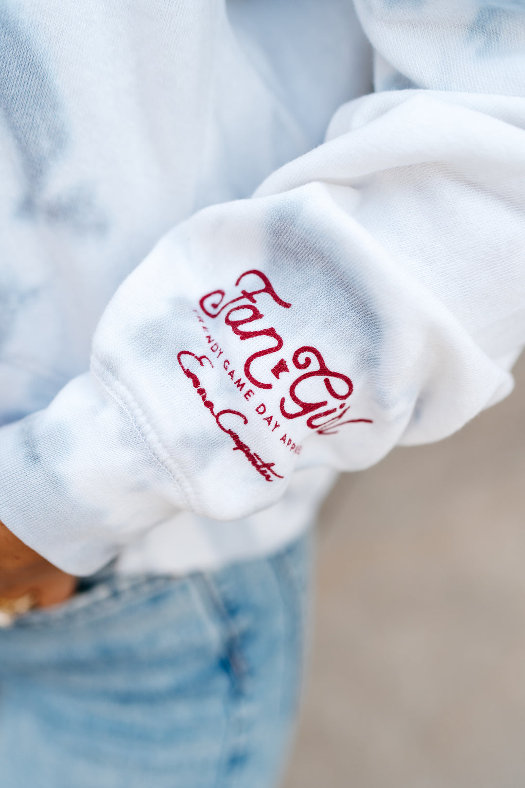 close up image of a sleeve of a tie dye hoodie with a maroon Fan Girl logo and Emma Carpenter's signature