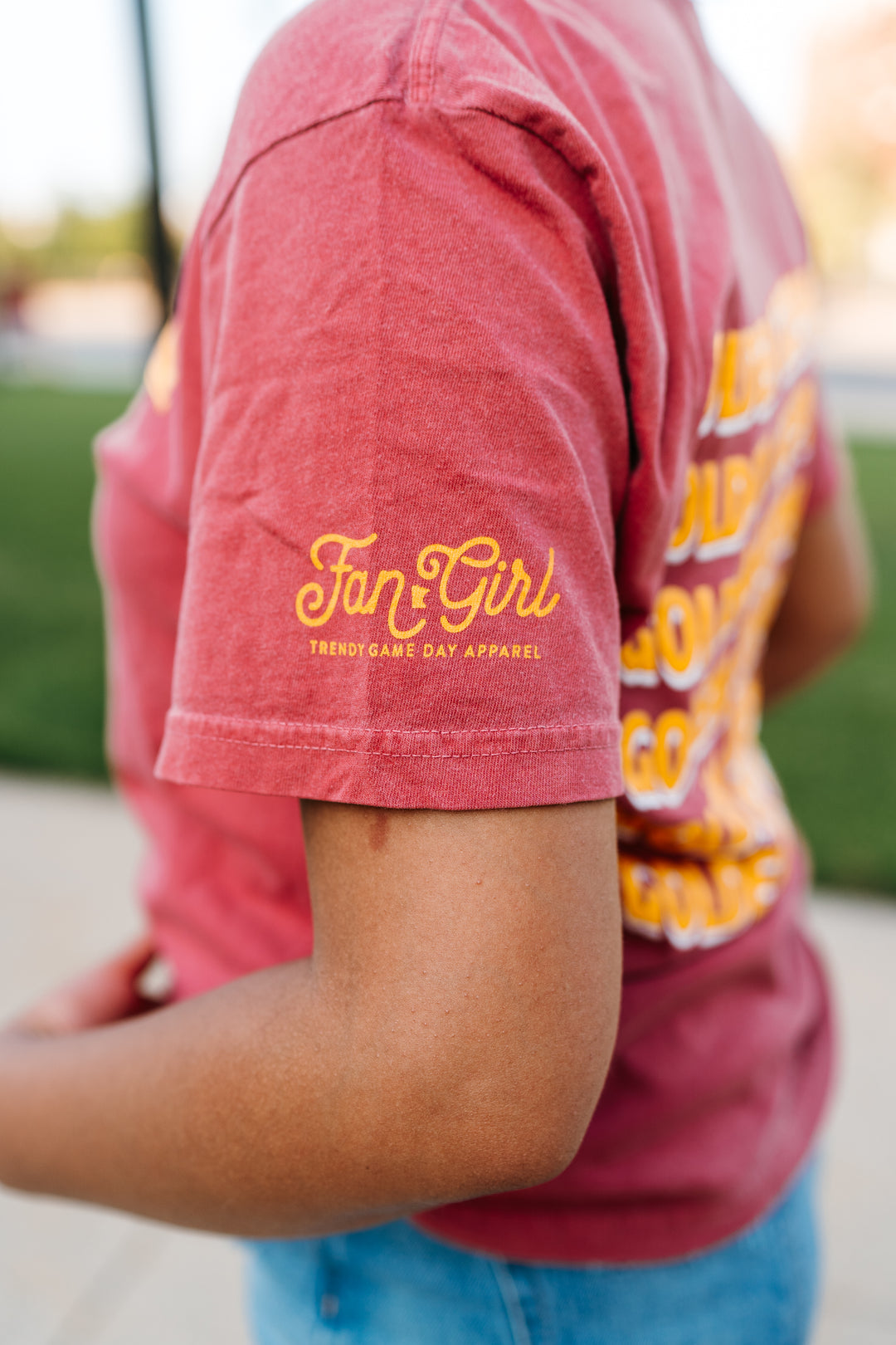 close up image of the left sleeve of crimson colored short sleeve with a Fan Girl logo screenprinted in gold