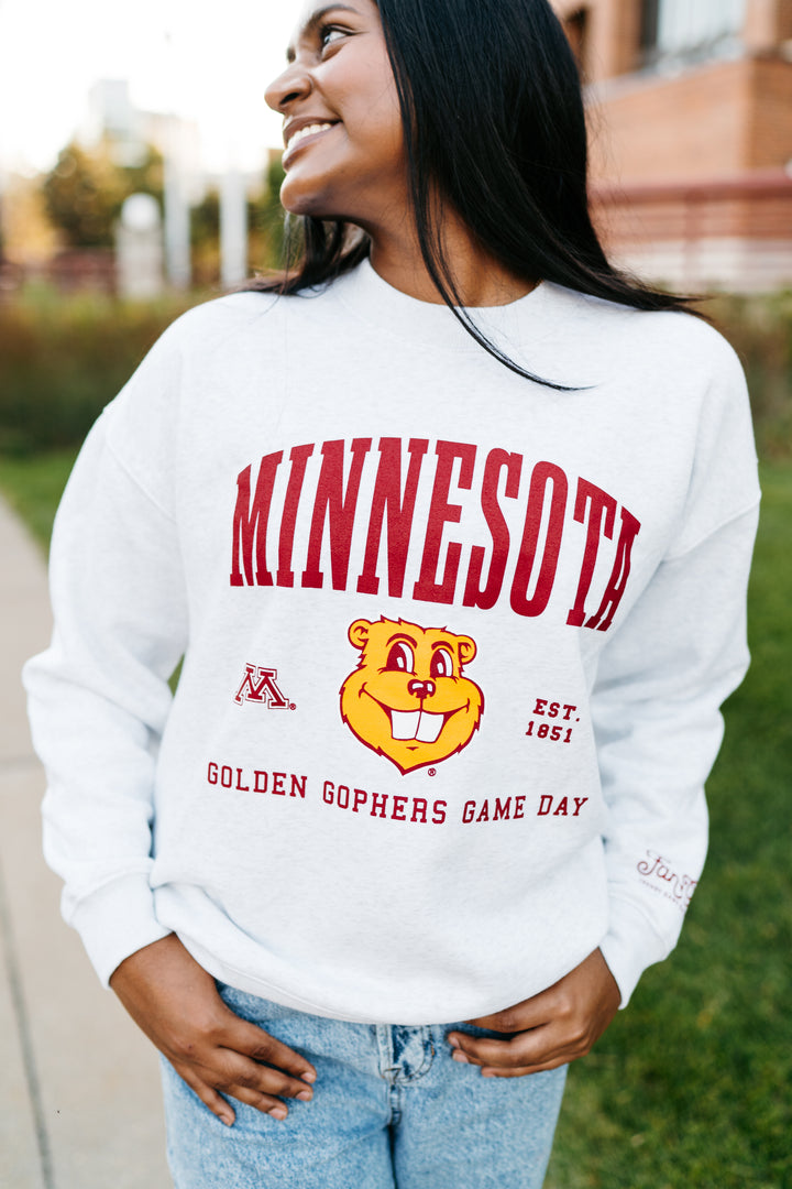 close up image of a girl outside wearing an ash gray crewneck with Minnesota screenprinted across the chest with a Goldy head graphic below in maroon and gold detail