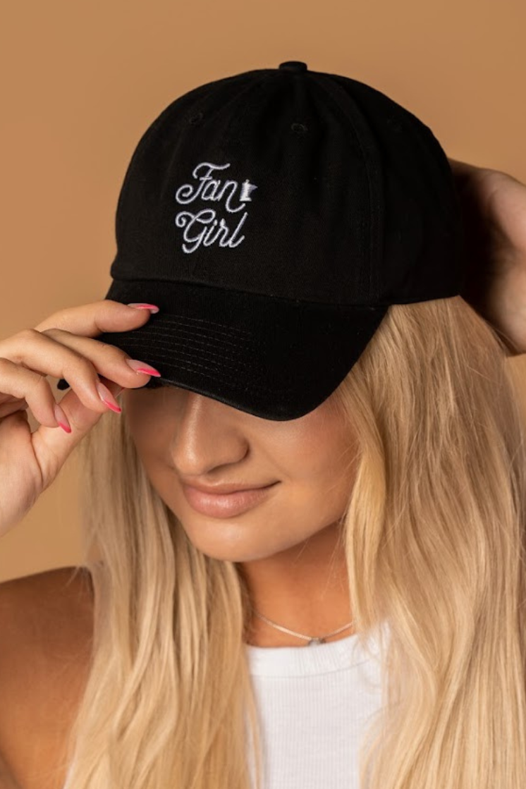 close up picture of a girl wearing a black baseball hat with a white embroidered Fan Girl logo 