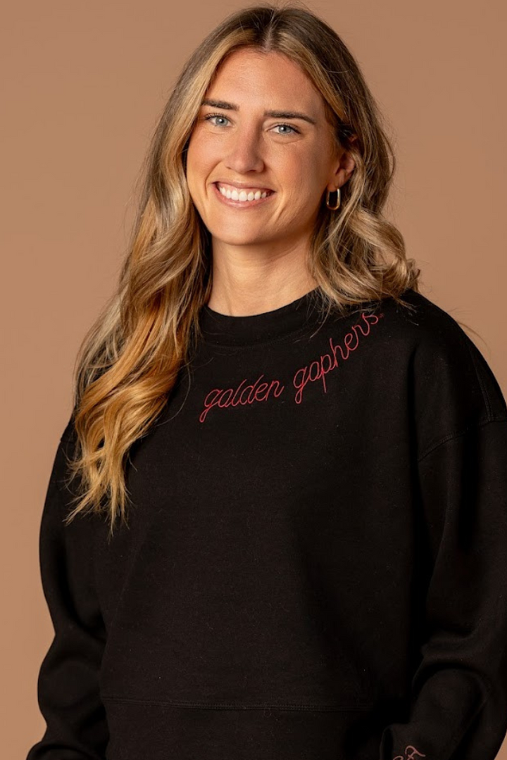 close up image of a girl wearing a black supersoft crewneck with golden gophers embroidered around the collar in maroon