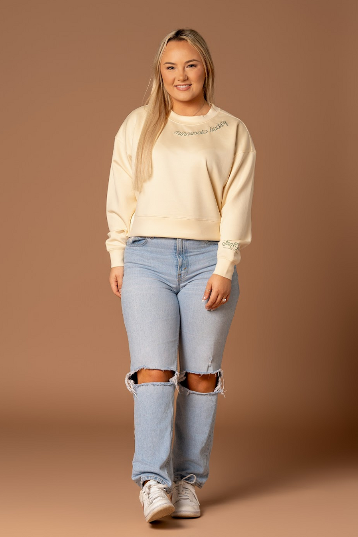 a farther away shot of a woman standing in an embroidered very soft ivory crew neck athleisure sweatshirt that says minnesota hockey