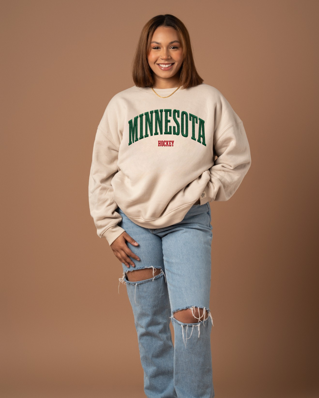 Person wearing a beige sweatshirt with 'MINNESOTA' printed on it against a brown background