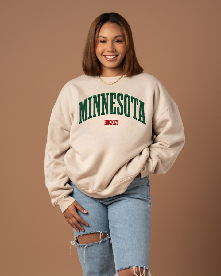 Person wearing a beige sweatshirt with 'MINNESOTA HOCKEY' text on a brown background