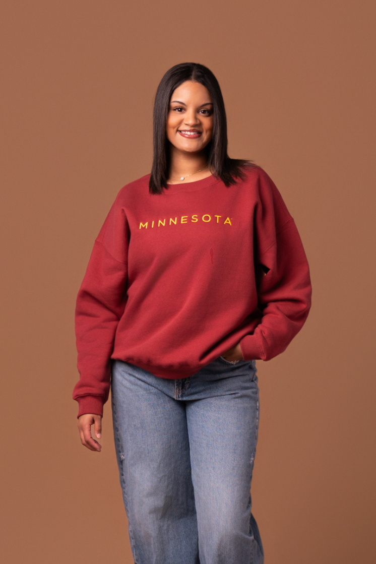 Woman wearing a maroon crew neck sweatshirt with yellow 'MINNESOTA' text