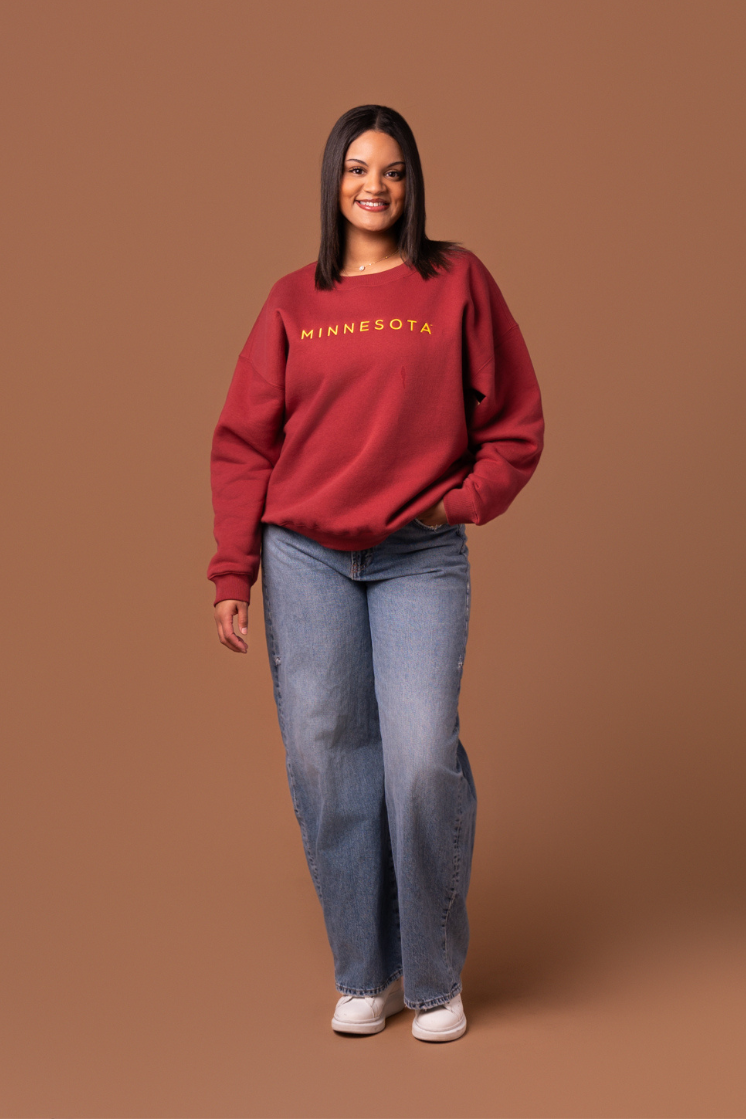 Woman wearing a maroon crew neck sweatshirt with yellow 'MINNESOTA' text