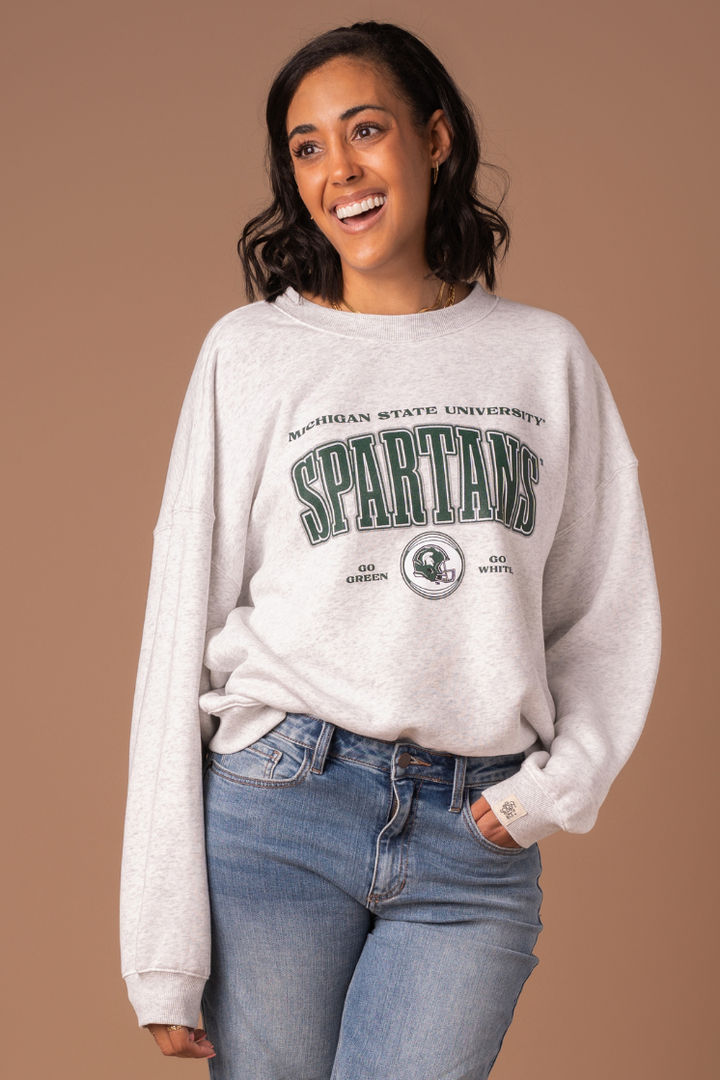 close up of a girl wearing a ash gray fleece lined Michigan State University Vintage Oversized Crew Neck sweatshirt with a green, black, and white screenprinted design