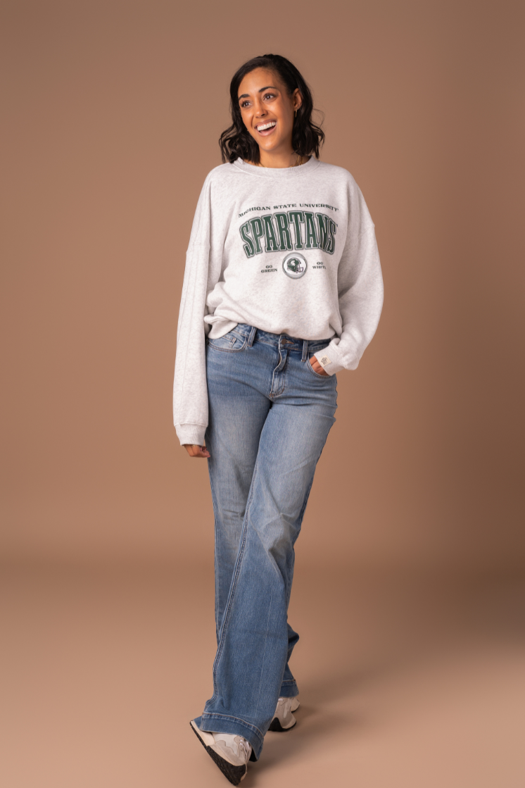 picture of a girl wearing a ash gray fleece lined Michigan State University Vintage Oversized Crew Neck sweatshirt with a green, black, and white screenprinted design