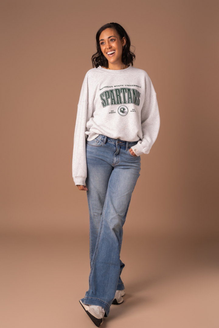 picture of a girl wearing a ash gray fleece lined Michigan State University Vintage Oversized Crew Neck sweatshirt with a green, black, and white screenprinted design