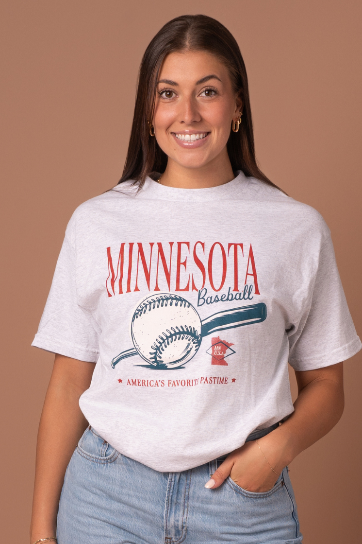 close up picture of a girl wearing a a vintage inspired ash gray cotton t-shirt with a minnesota baseball design with blue and red screenprinted details 