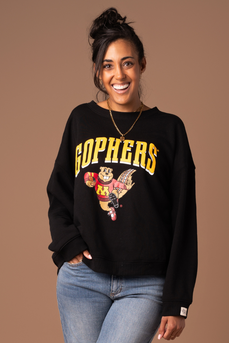 close up image of girl wearing a black crewneck with Gophers screenprinted in gold across the chest with a Goldy graphic holding a football in maroon and gold decoration