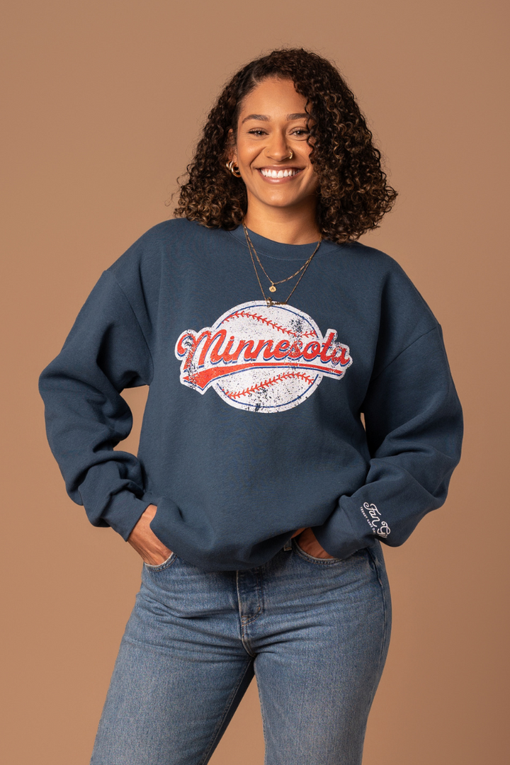 close up picture of a girl wearing a navy fleece-lined navy crew neck sweatshirt with a screenprinted minnesota baseball design