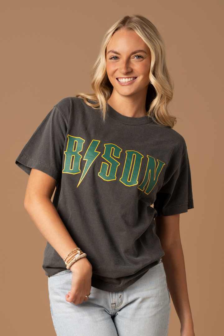 close up image of a girl wearing a faded black tee with the word Bison screenprinted, except the "i" is a lightning in green color with gold outline