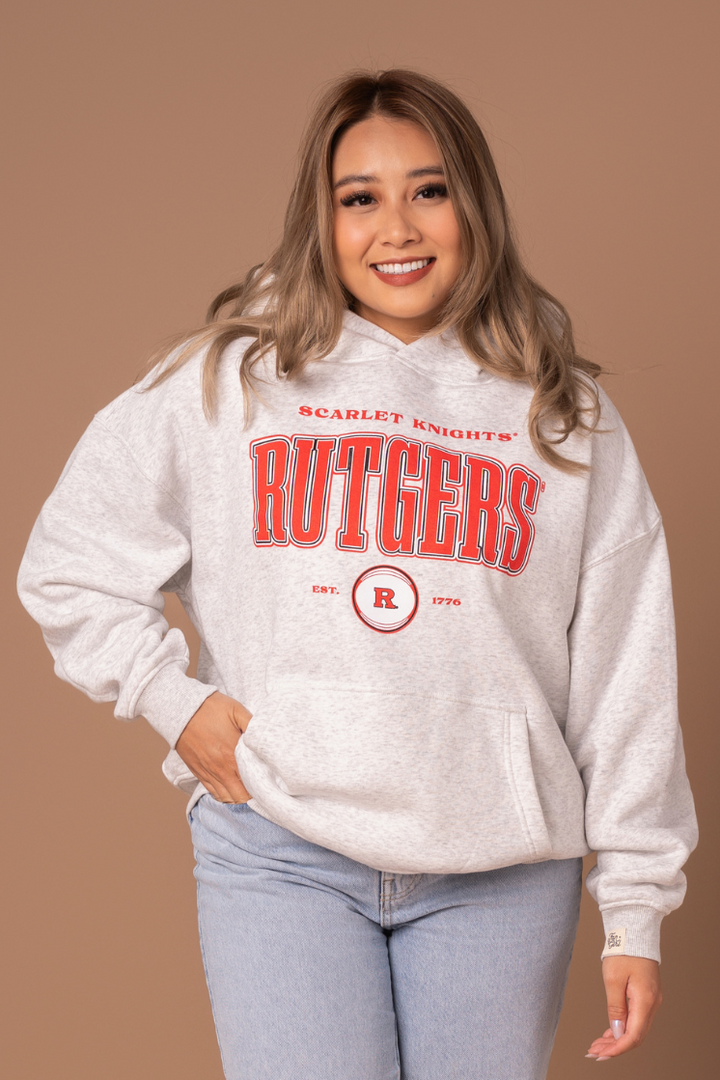 close up picture of a girl in a ash gray hoodie with a vintage inspired red, black, and white Rutgers University screenprinted design 