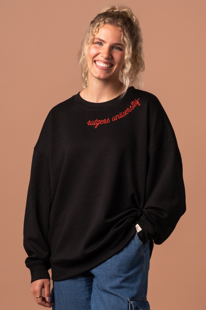 close up of a girl wearing a black  Supersoft Crew Neck, an athleisure material with red embroidered detail that says "Rutgers University"