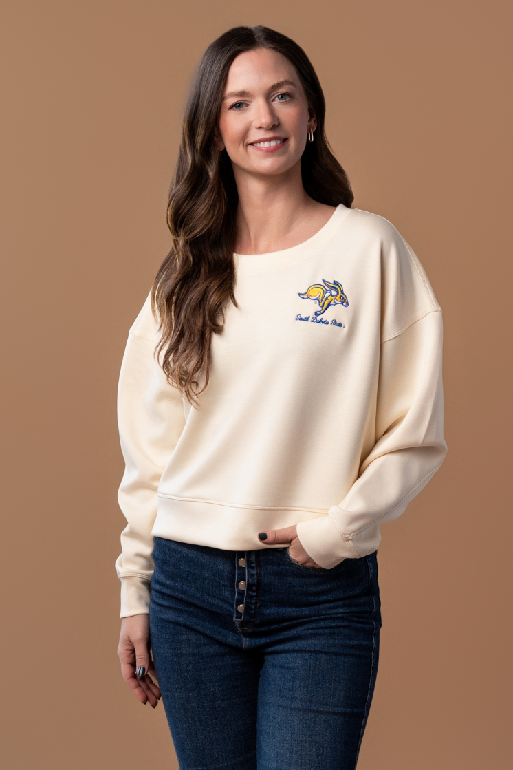 close up image of a girl wearing a bone colored crewneck with an embroidered SDSU Jackrabbits logo in the left side of the pocket