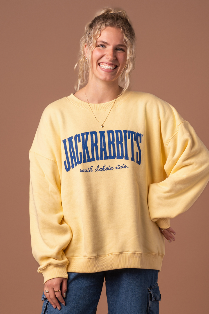 close up image of a girl wearing a yellow crewneck with Jackrabbits written across the chest in blue and south dakota state written in cursive in blue underneath