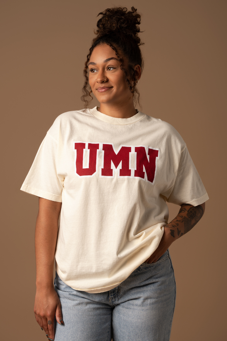 close up image of a girl wearing a cream tshirt with UMN screenprinted in block letters in maroon with a white outline