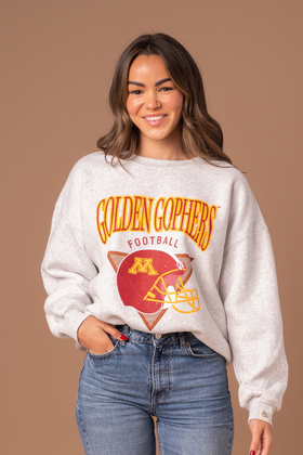 close up image of a girl wearing an ash gray crewneck with Golden Gophers Football screenprinted with a distressed football graphic in maroon and gold 