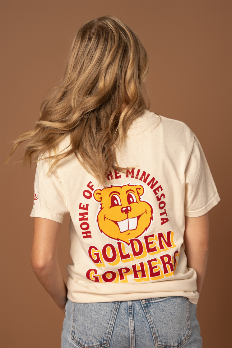 close up image of the back of a girl wearing a cream colored t-shirt with a Goldy graphic screenprinted in the center with Home of the Minnesota Golden Gophers outline in maroon and gold 