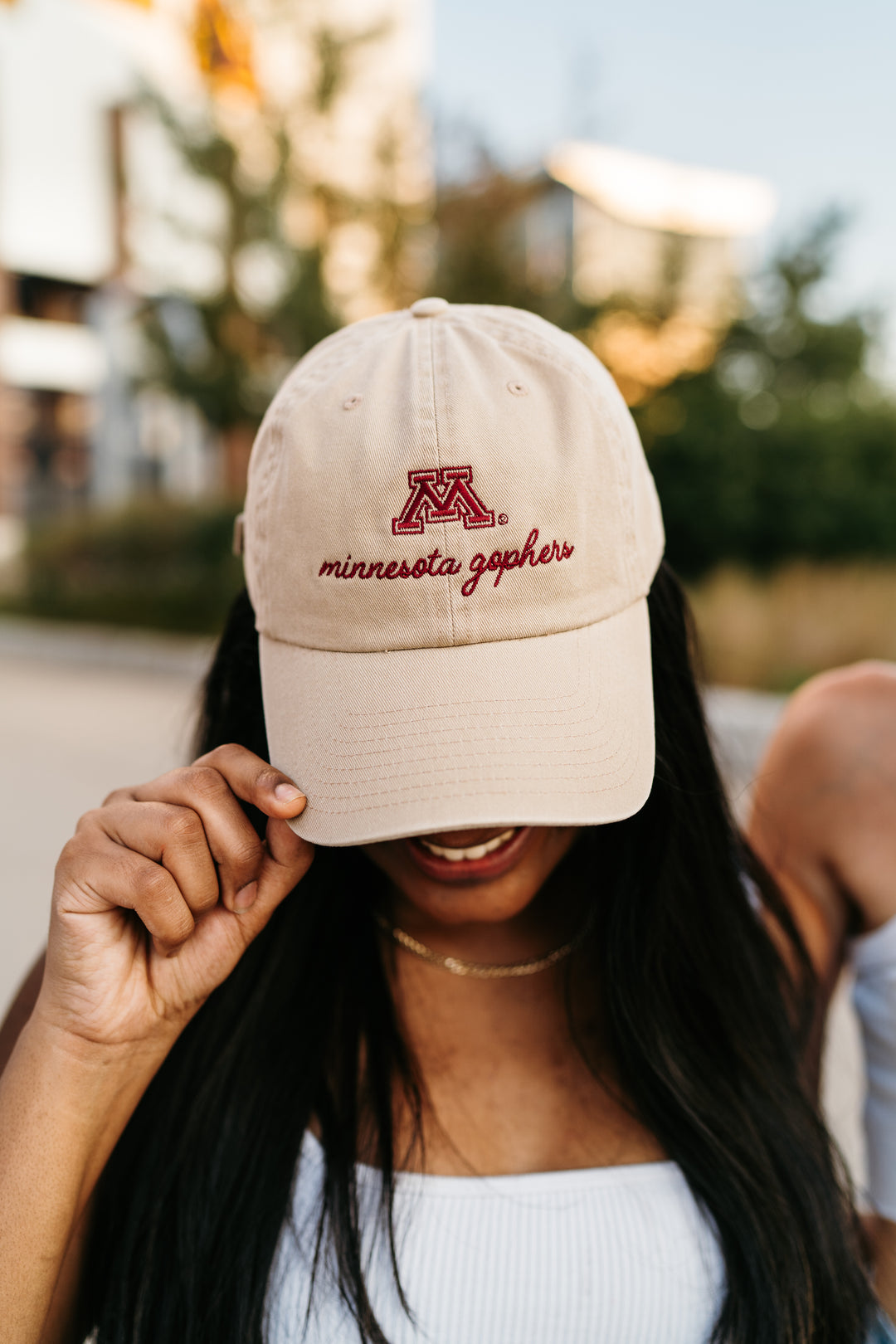 close up image of girl outside wearing a tan hat with an M and minnesota gophers embroidered in cursive in maroon