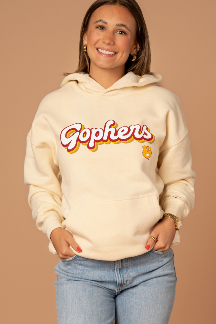 close up image of a girl wearing an ivory colored hoodie with a Gophers screenprint in a retro font with maroon and gold outlines with a Goldy head below it in gold