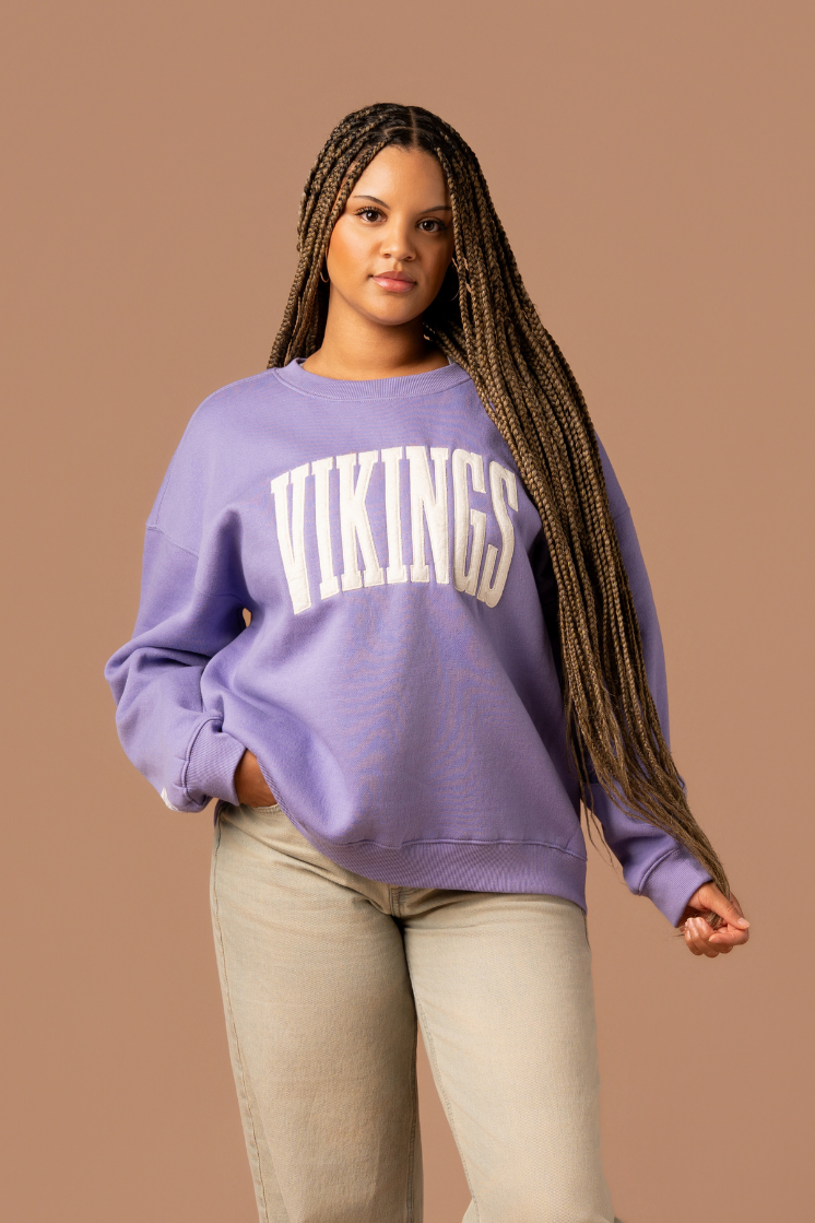 Woman wearing a purple crew neck sweatshirt with large, cream 'Vikings' text