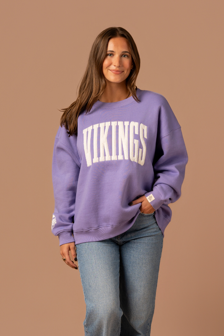 Woman wearing a purple crew neck sweatshirt with large, cream 'Vikings' text