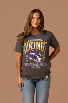 Woman wearing a faded black t-shirt with gold and purple 'Minnesota Vikings Football Club' and 'EST. 1961' text with a purple Vikings helmet graphic in the center 