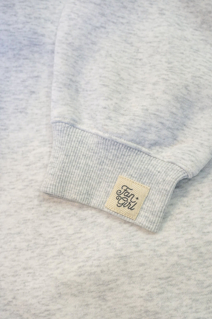 Close-up of a heather gray crew neck sweatshirt with a brand tag on the sleeve