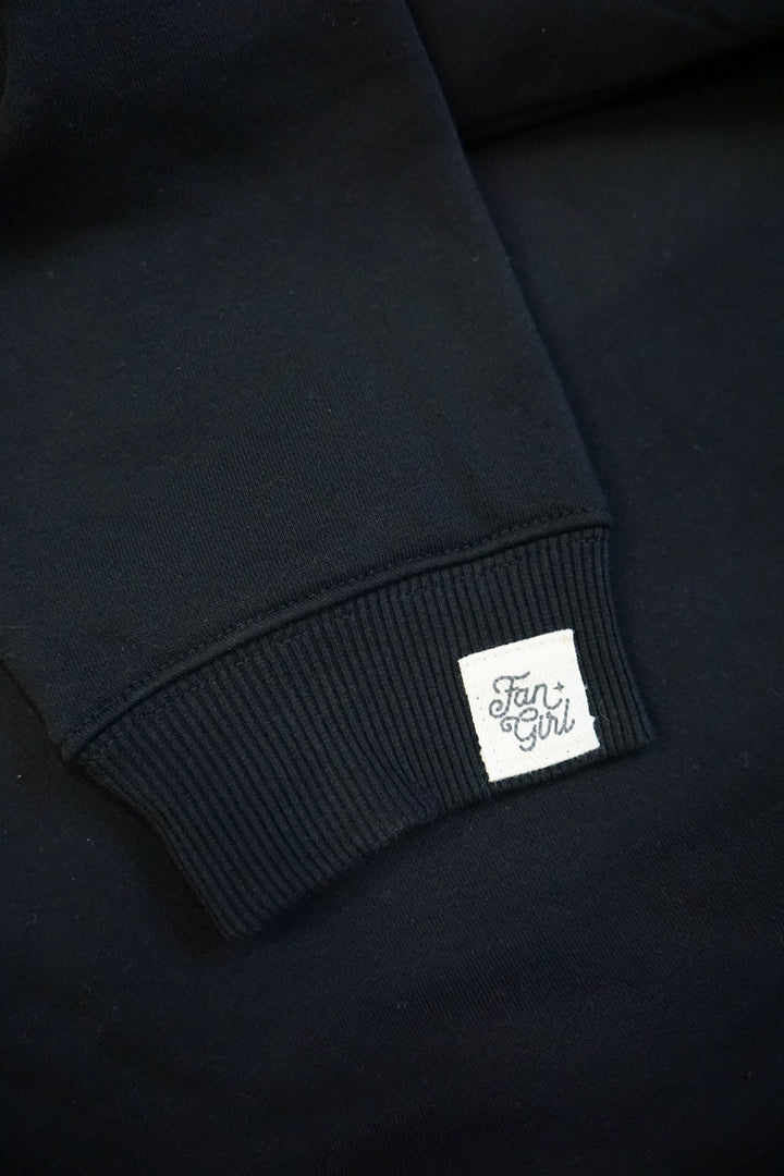 close up of the sleeve of a black crew neck sweatshirt with a branded tag