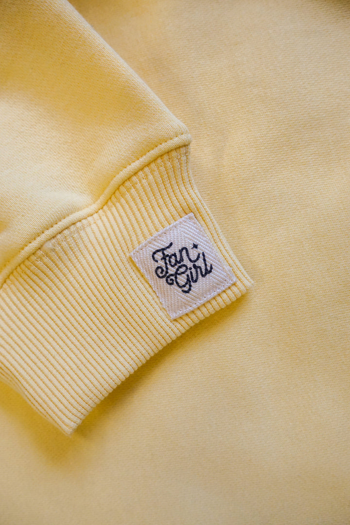 Close-up of a yellow crew neck sweatshirts sleeve with a "Fan Girl" branded logo 