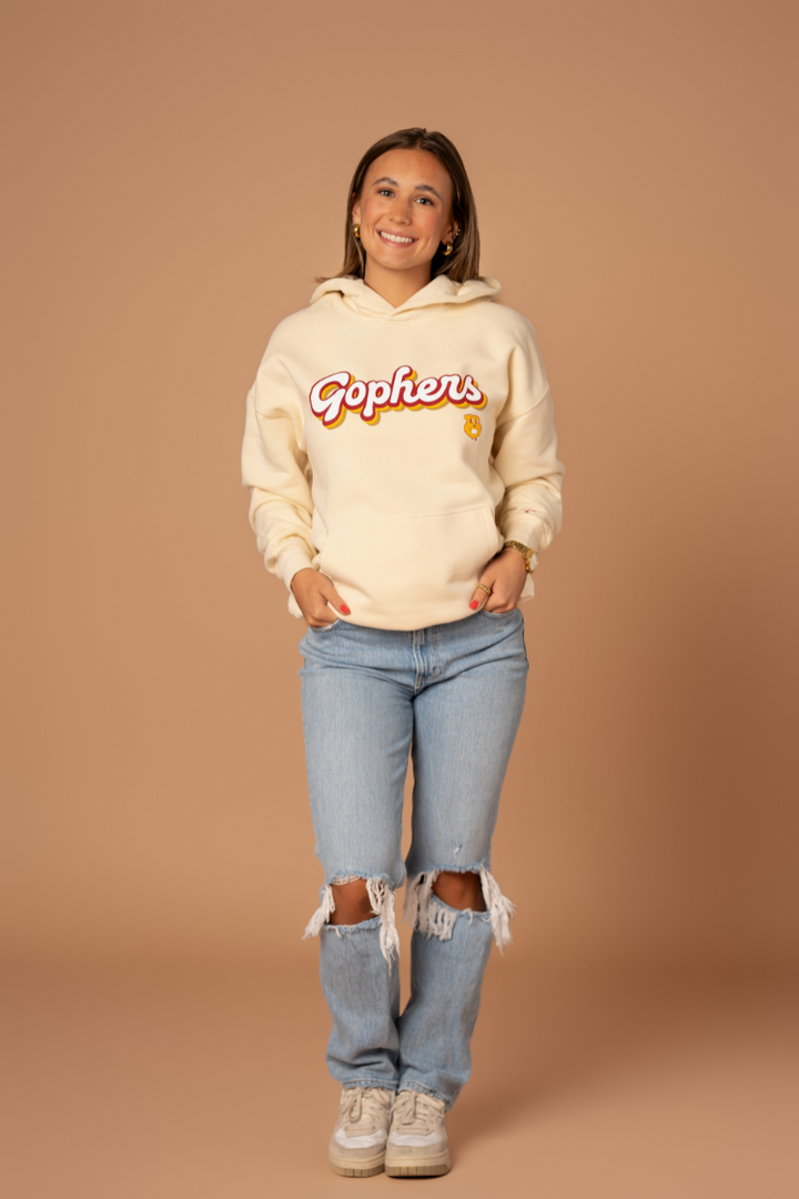 full body image of a girl wearing jeans and an ivory colored hoodie with a Gophers screenprint in a retro font with maroon and gold outlines with a Goldy head below it in gold