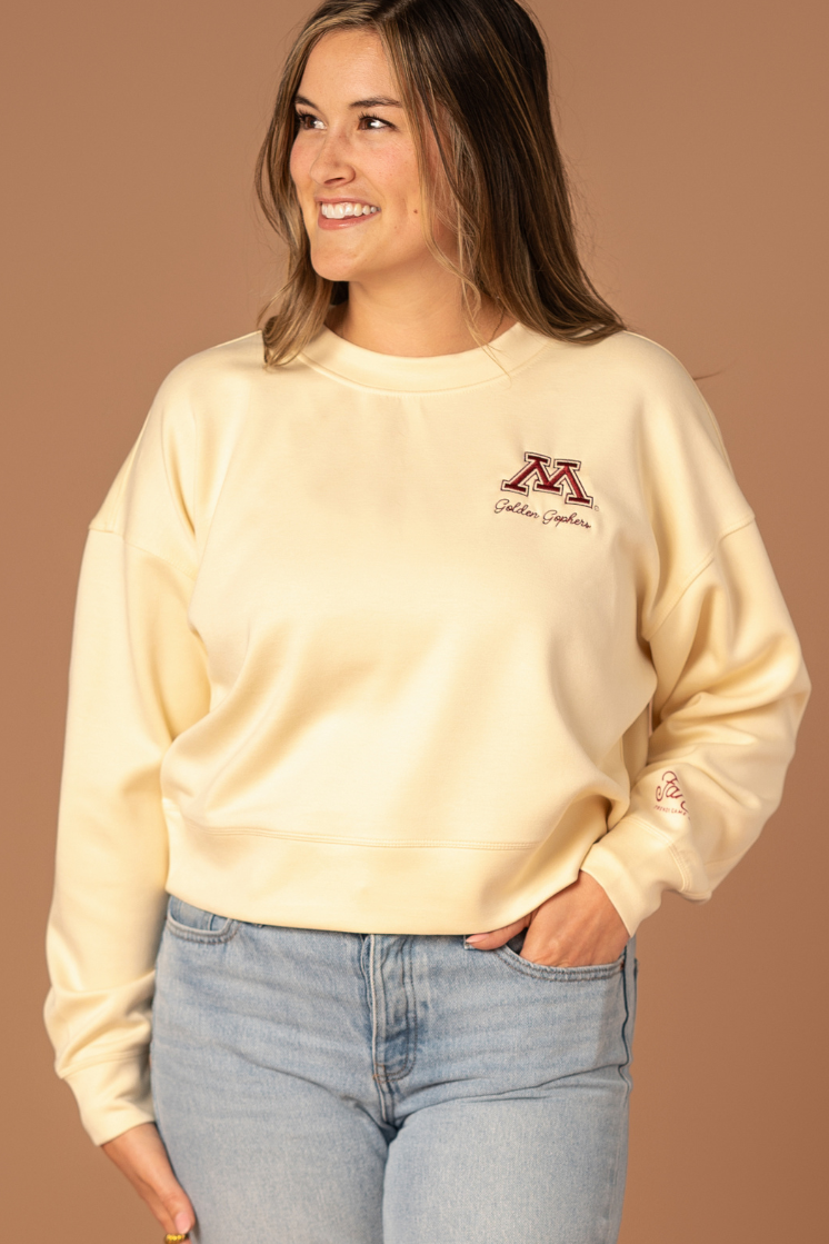 close up image of a girl wearing a bone colored supersoft crewneck with a M logo and Golden Gophers embroidered in maroon on the left side pocket of the crew