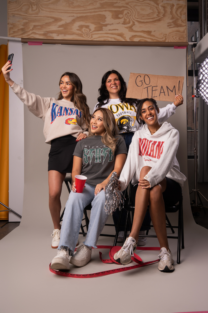 image of 4 girls posing together pretending they are at a college tailgate and are representing 4 different schools including a University of Kansas crewneck