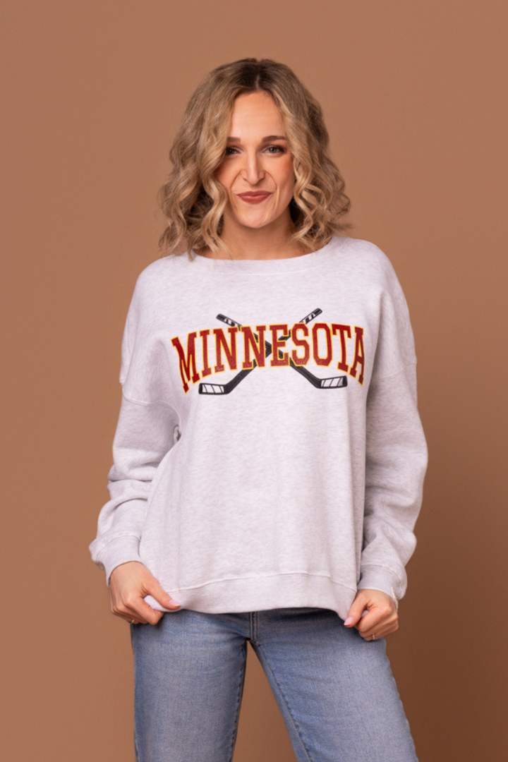 woman in a heather gray crew neck sweatshirt with maroon "minnesota" text and two black hockey sticks