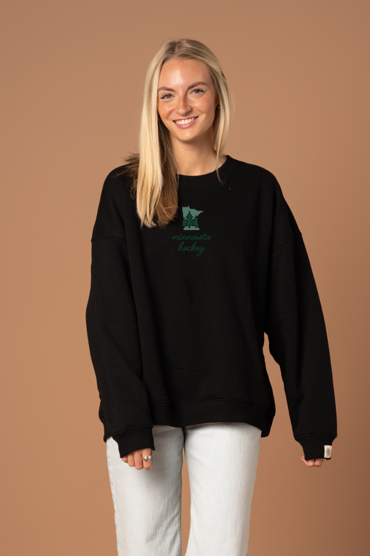 woman in black crew neck sweatshirt with green "minnesota hockey" cursive text and a small green minnesota state graphic with trees on it