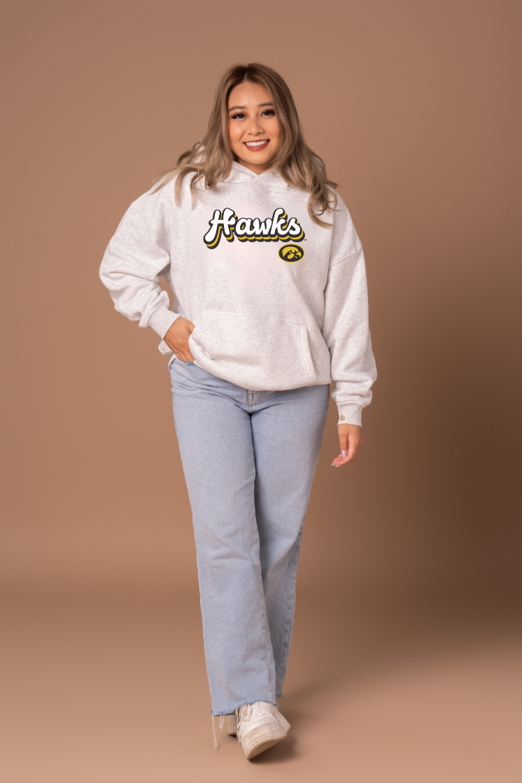 Woman wearing a heather grey hoodie with 'Hawks' text and a Hawkeye logo