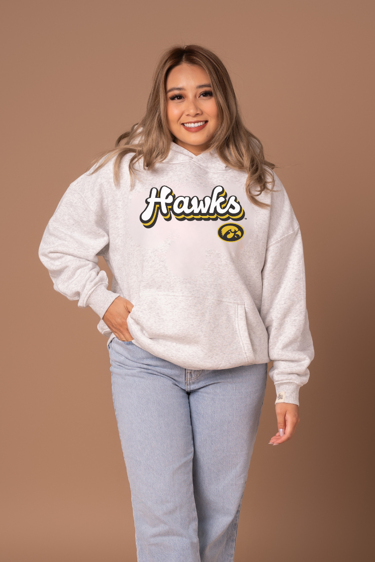 Woman wearing a heather grey hoodie with 'Hawks' text and a Hawkeye logo