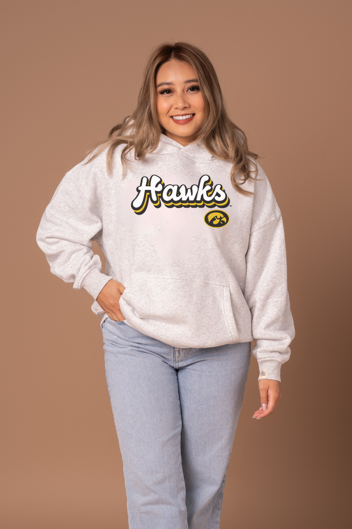 Woman wearing a heather grey hoodie with 'Hawks' text and a Hawkeye logo