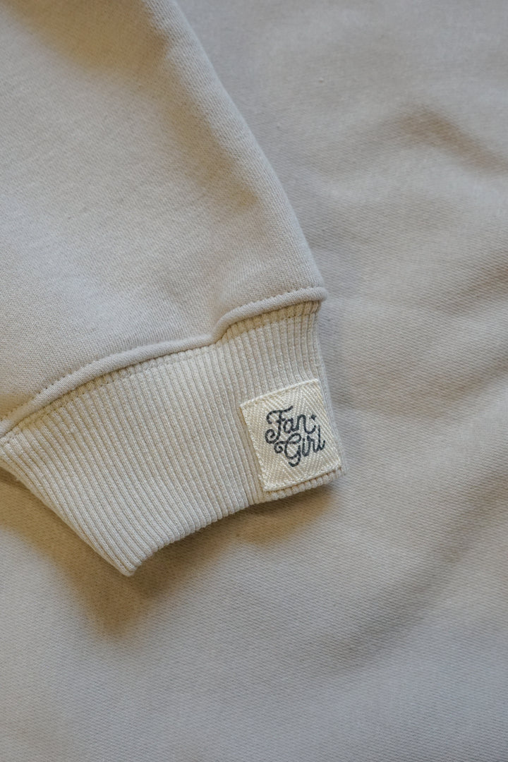 Close-up of a beige sweatshirt with a brand label on the sleeve.