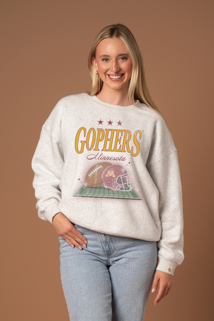Woman wearing a ash gray crew neck sweatshirt with 'Gophers Minnesota' text and a football and helmet graphic under it