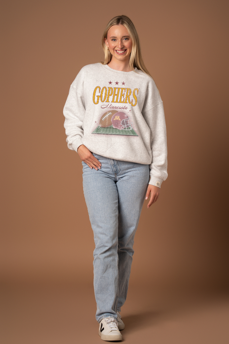 Woman wearing a ash gray crew neck sweatshirt with 'Gophers Minnesota' text and a football and helmet graphic under it