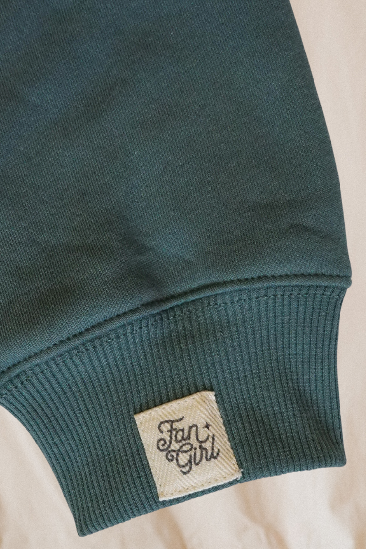 Close-up of a green crew neck sweatshirt sleeve with a 'Fan Girl' branded label 