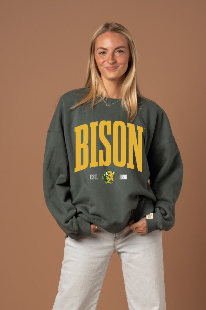 Woman wearing a green crew neck sweatshirt with 'BISON' text in yellow with a Bison logo under it
