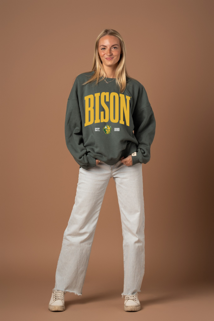 Woman wearing a green crew neck sweatshirt with 'BISON' text in yellow with a Bison logo under it