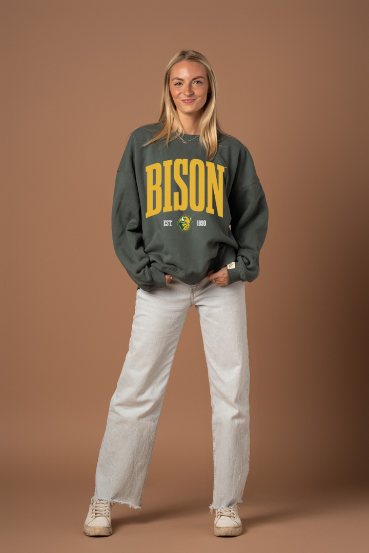 Woman wearing a green crew neck sweatshirt with 'BISON' text in yellow with a Bison logo under it