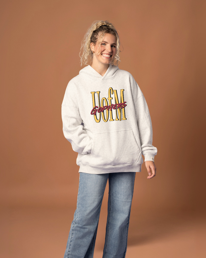 Woman wearing a heather grey hoodie with 'U of M Gophers' text in yellow and maroon