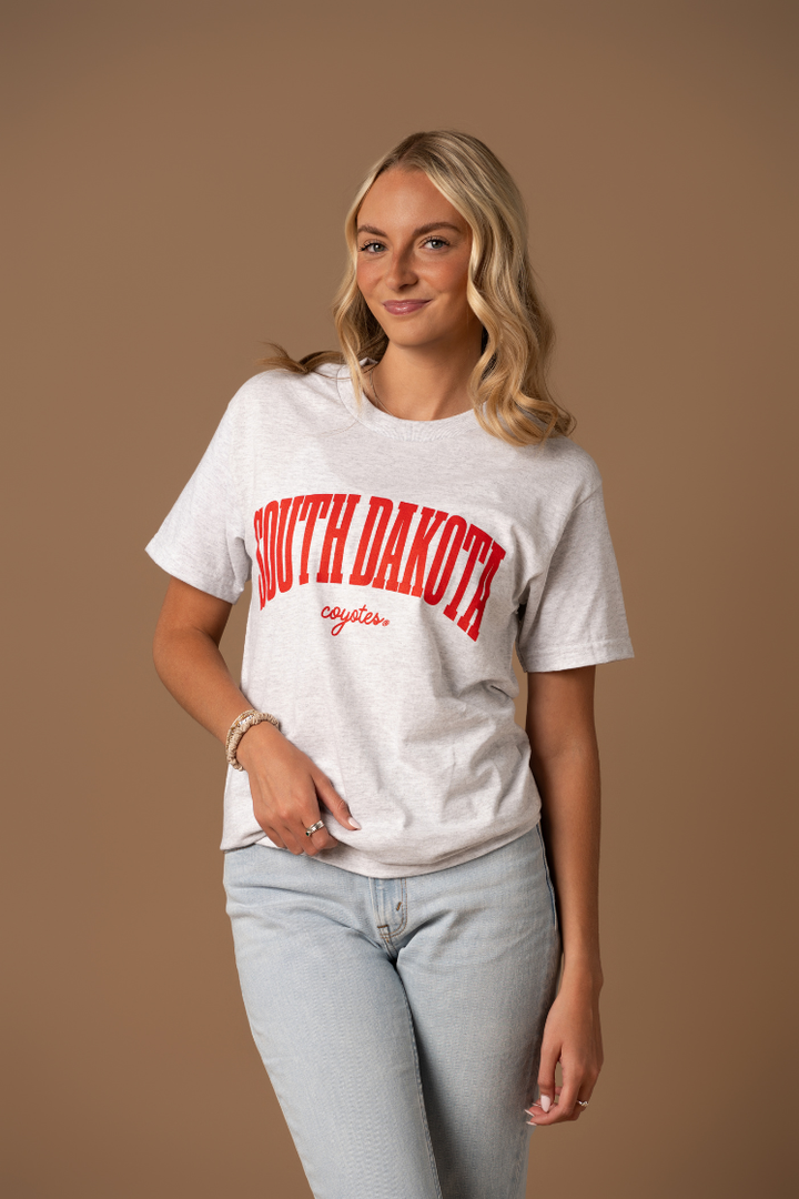 Woman wearing an ash gray tee with South Dakota Coyotes written in cursive in red