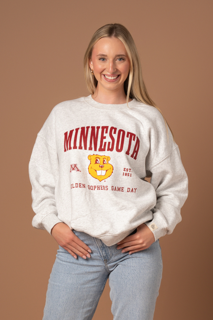 Woman wearing an ash gray crewneck with Minnesota screenprinted across the chest with a Goldy head graphic below in maroon and gold detail